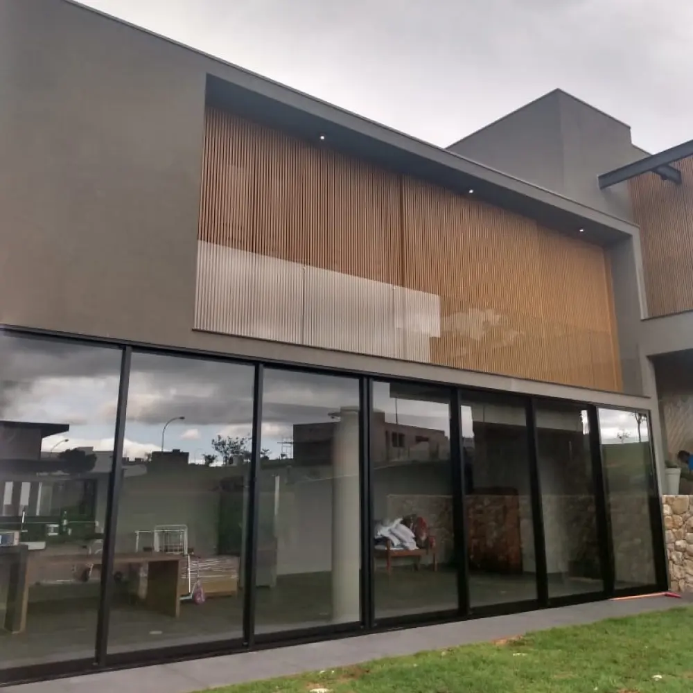 Fachada com térreo todo envidraçado em perfil preto e volume superior em ripado de madeira